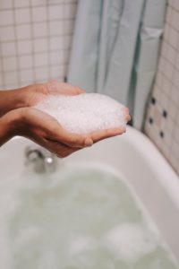 bubbles in hands above a bathtub filling with water