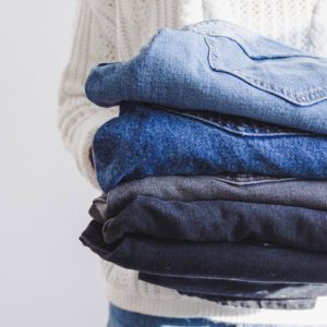 Close up stack of folded jeans being held by a person in a white sweater.