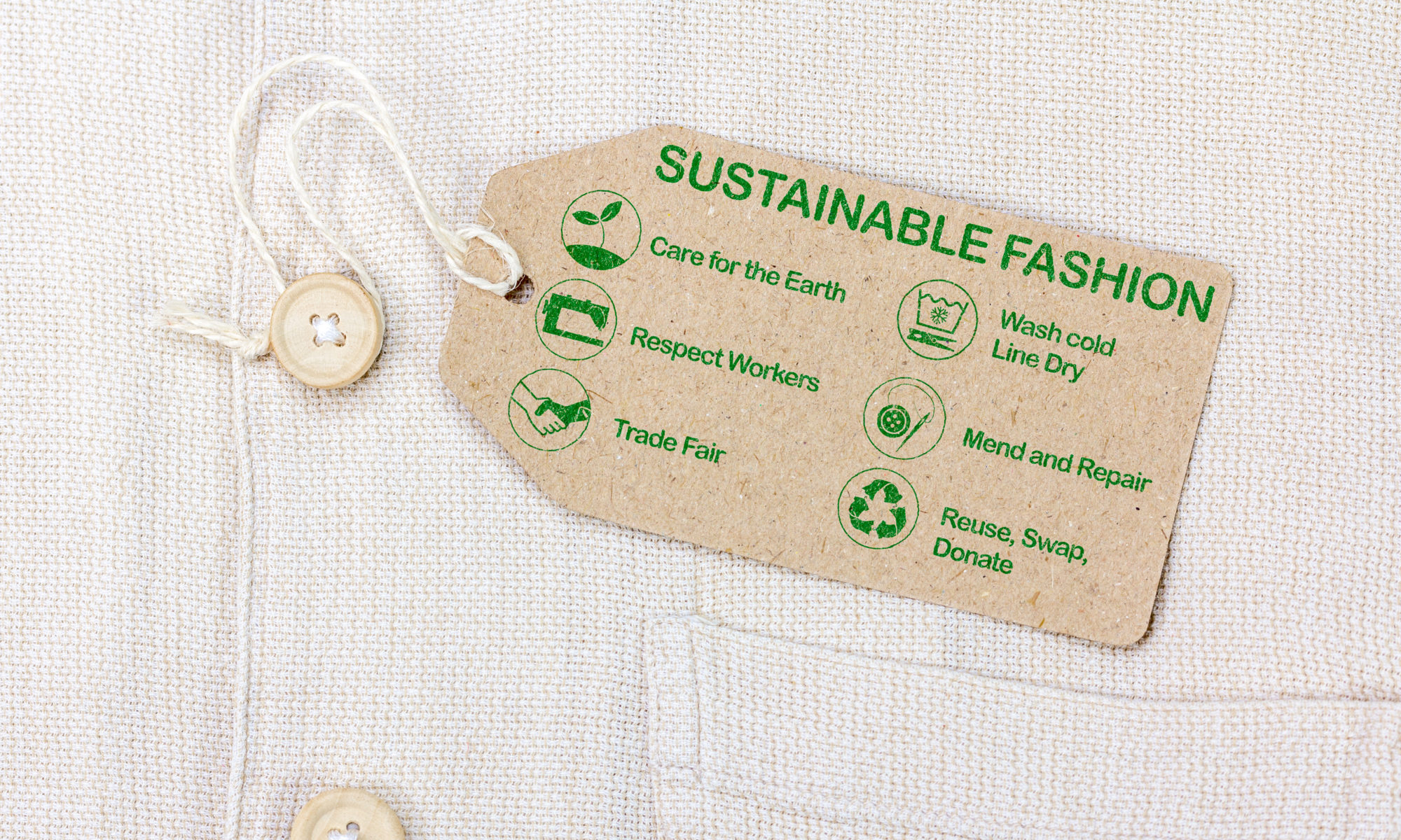 Tag attached to linen shirt with paper tag that reads, in green print: Sustainable Fashion across the top and then below with icons for each item, Care for the Earth, Wash cold Line Dry, Respect Workers, Mend and Repair, Trade Fair, Reuse, Swap, Donate