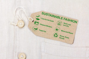 Tag attached to linen shirt with paper tag that reads, in green print: Sustainable Fashion across the top and then below with icons for each item, Care for the Earth, Wash cold Line Dry, Respect Workers, Mend and Repair, Trade Fair, Reuse, Swap, Donate
