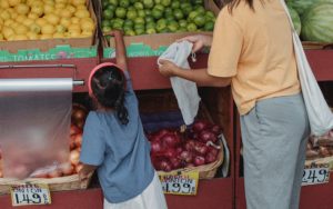 Young girl grabbing limes in a market with woman holding out a fabric produce bag