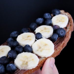 close up of blueberries and sliced bananas on a piece of wheat toast with a nut butter smear