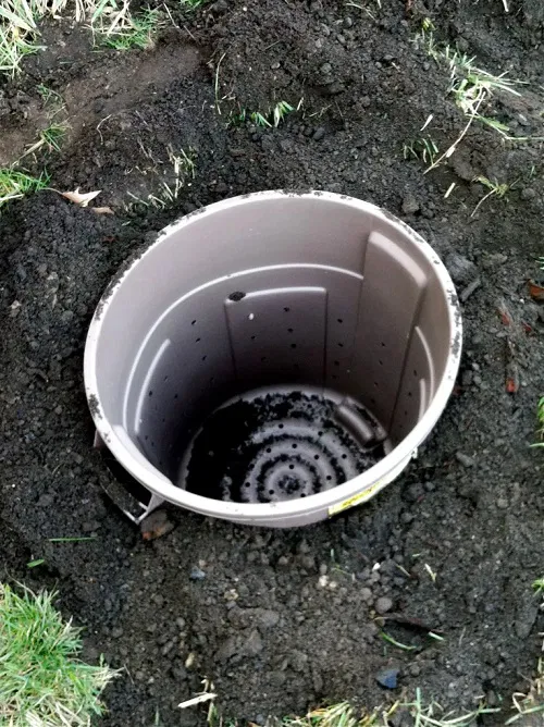 This trash can has holes poked in it and is sunk into the ground to make a easy DIY compost receptacle.